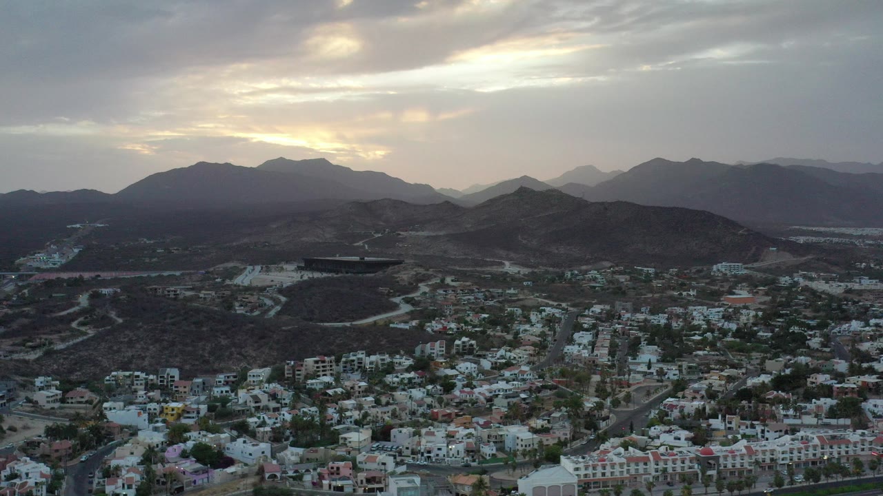 Aerial view of hillside buildings below dark mountains and cloudy sky.