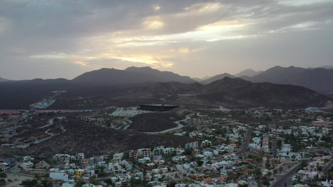 Aerial view of a town below dark mountain ridges and a cloudy sky.