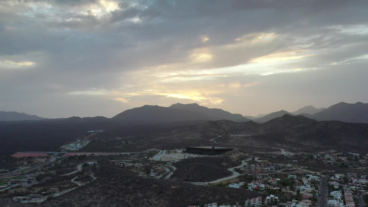 Wide aerial view of mountains, town roads, and cloudy sky.