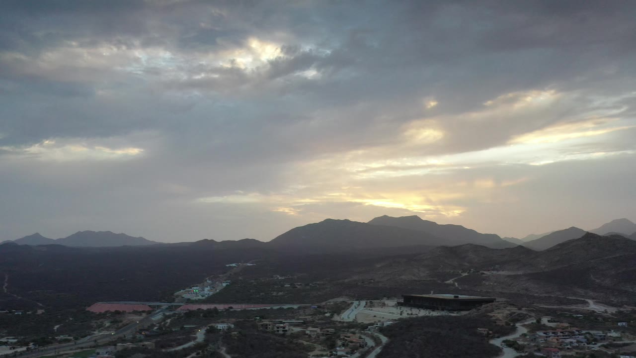 Drone perspective over roads and desert hills with mountains on the horizon.