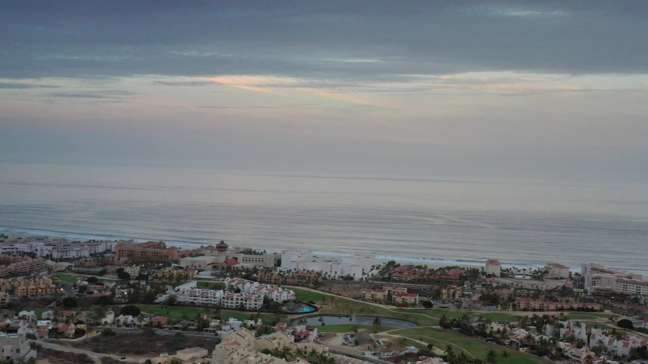 Aerial view of coastal buildings beside a wide ocean under layered clouds.