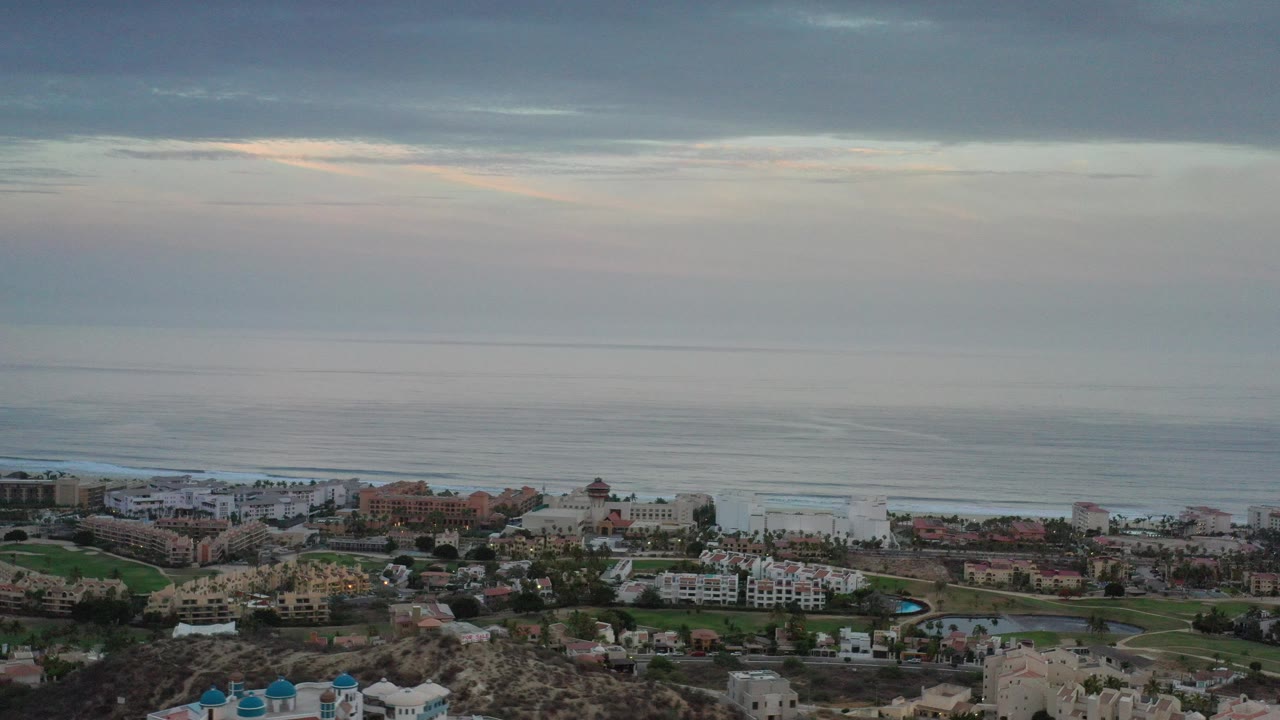 Elevated coastal view with ocean, buildings, and cloudy sky.