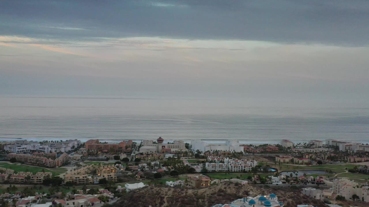 Coastal buildings and ocean under layered clouds.