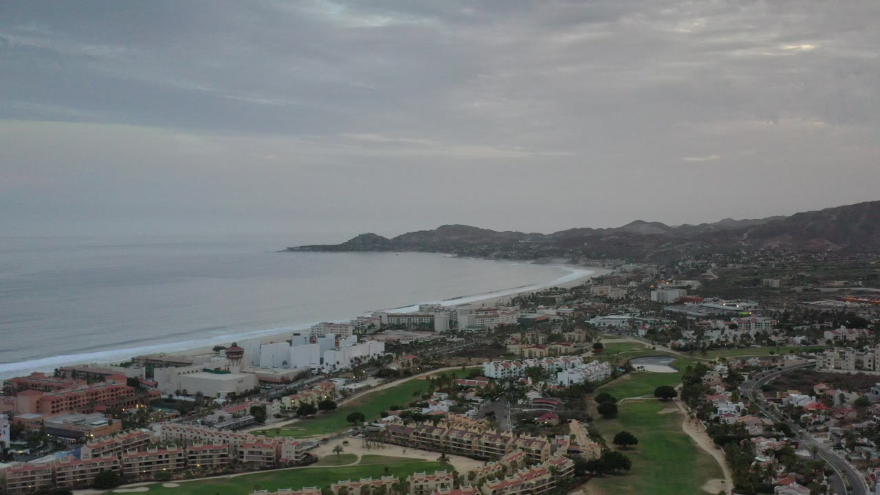 Aerial view of coastline, city buildings, beach, hills, and gray clouds.