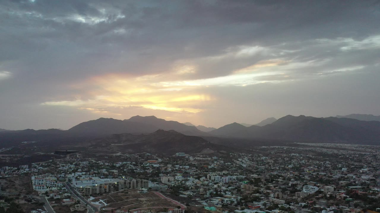 Aerial dusk view of a city below mountains and clouds.