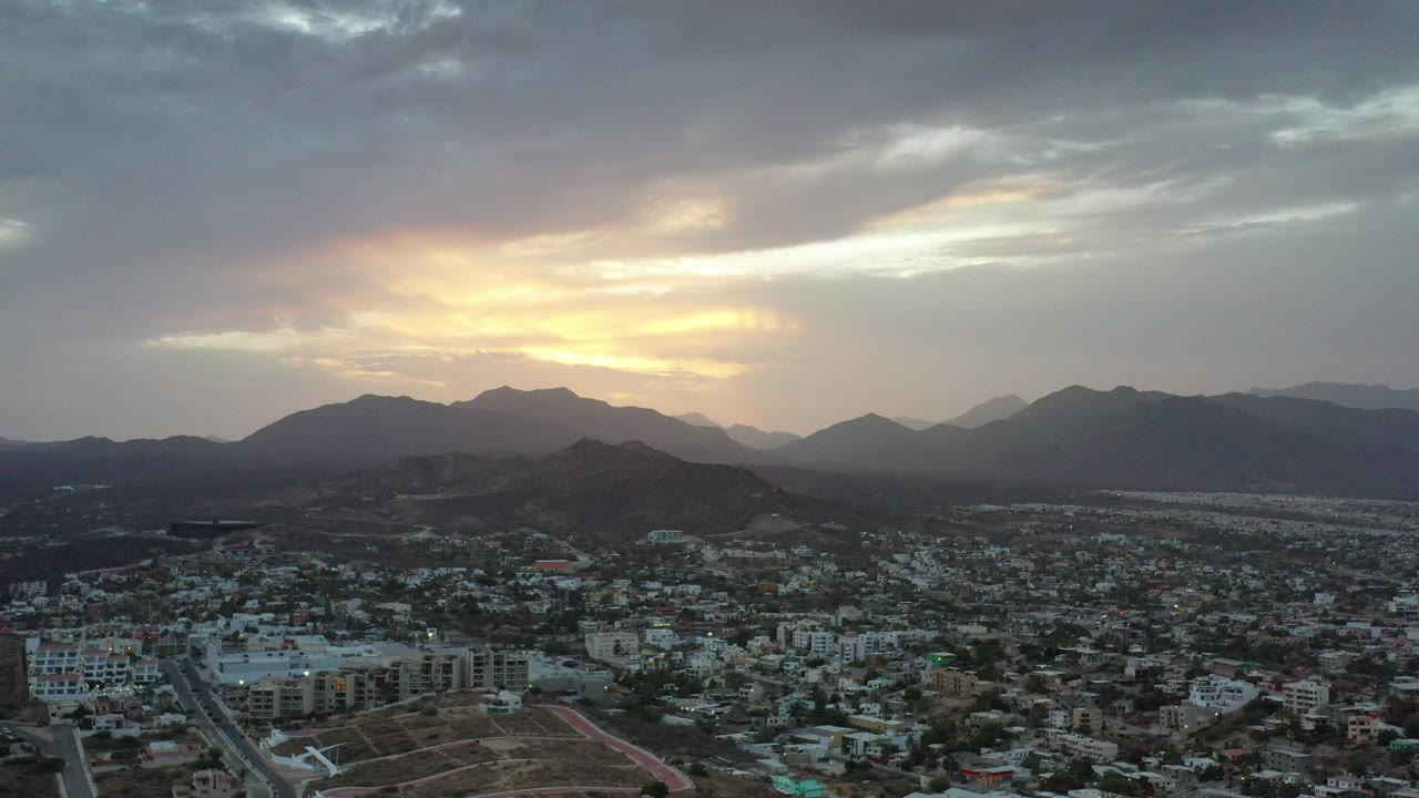 Aerial cityscape below dark mountain ridges at sunset.