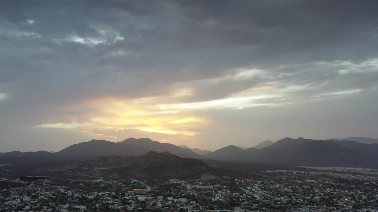 Aerial view of city rooftops below mountains at sunset