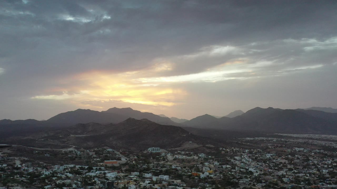Sunrise glow behind mountain ridges above a low cityscape.