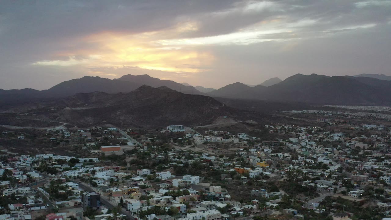 Los Cabos rooftops and hills beneath gray sunset clouds