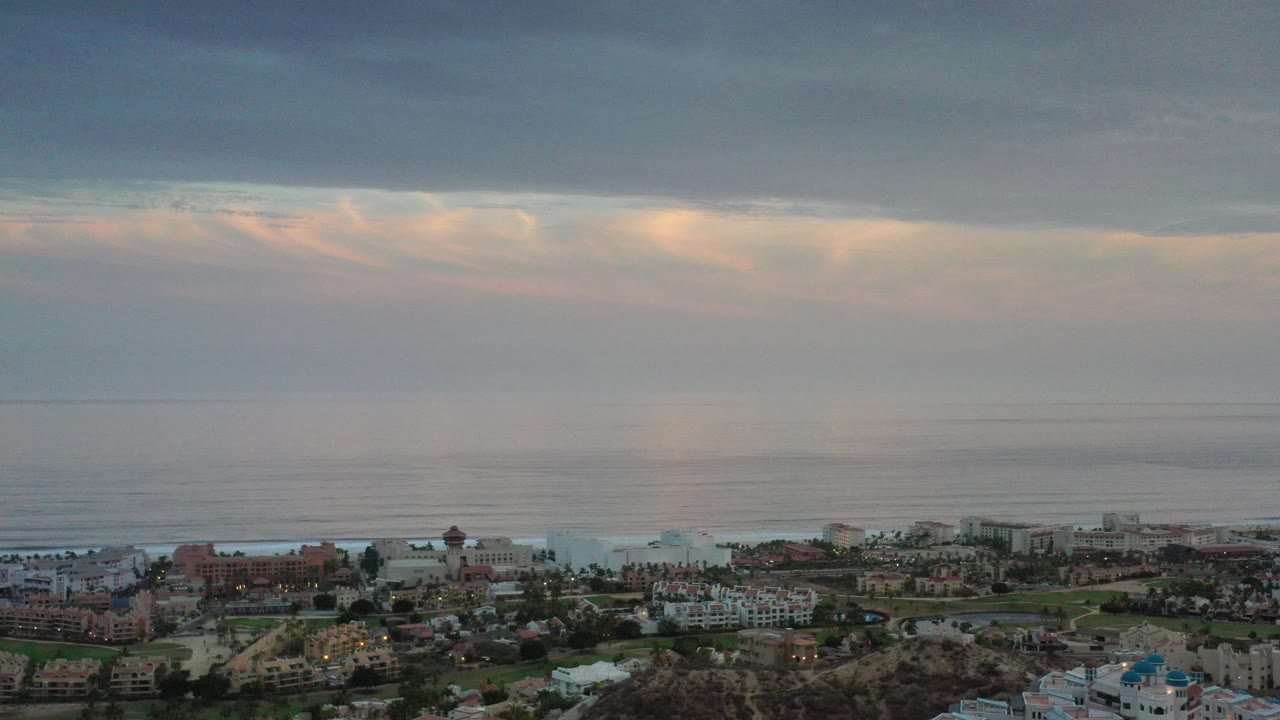 Elevated coastal view with ocean, clouds, and beachfront buildings.