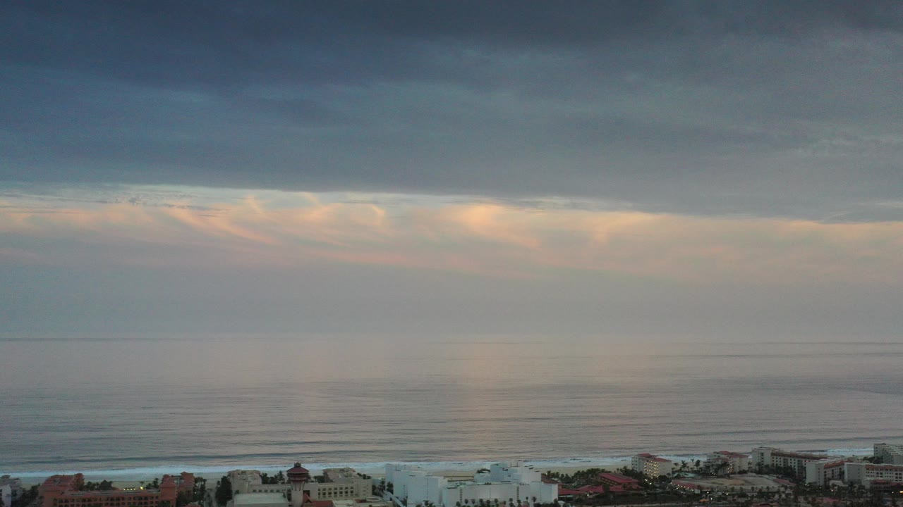 Dark clouds over a calm ocean horizon with coastal buildings below