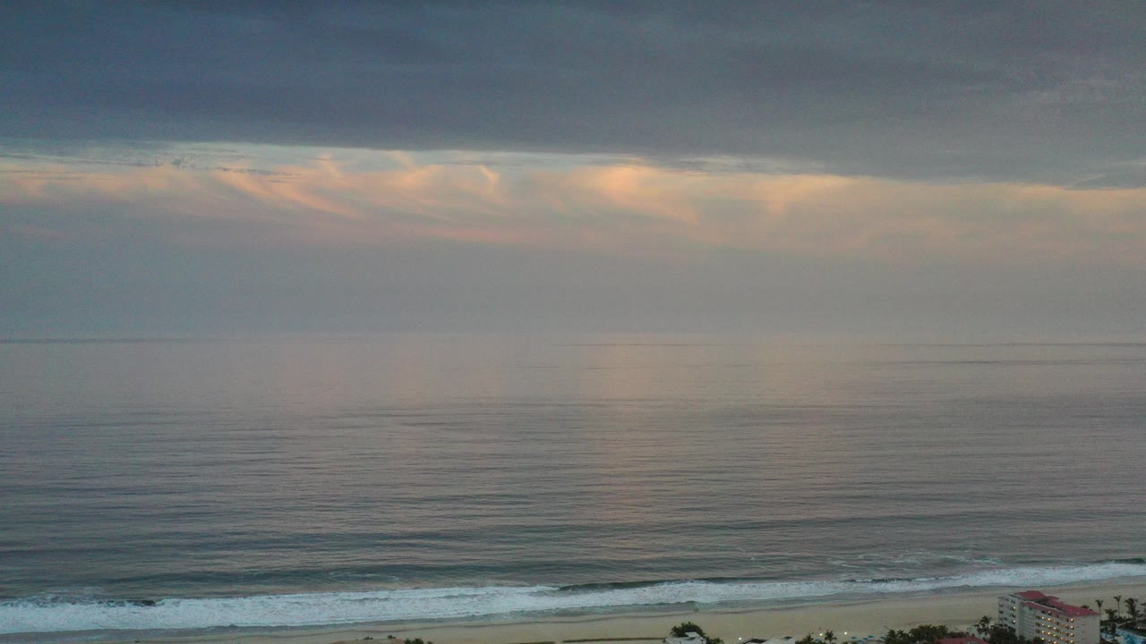 Wide ocean horizon under dark clouds with surf near the shore.