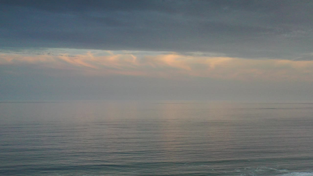 Opening frame of the Los Cabos ocean with gray water, a level horizon, dark overhead clouds, pale warm light near the skyline, and no visible people.