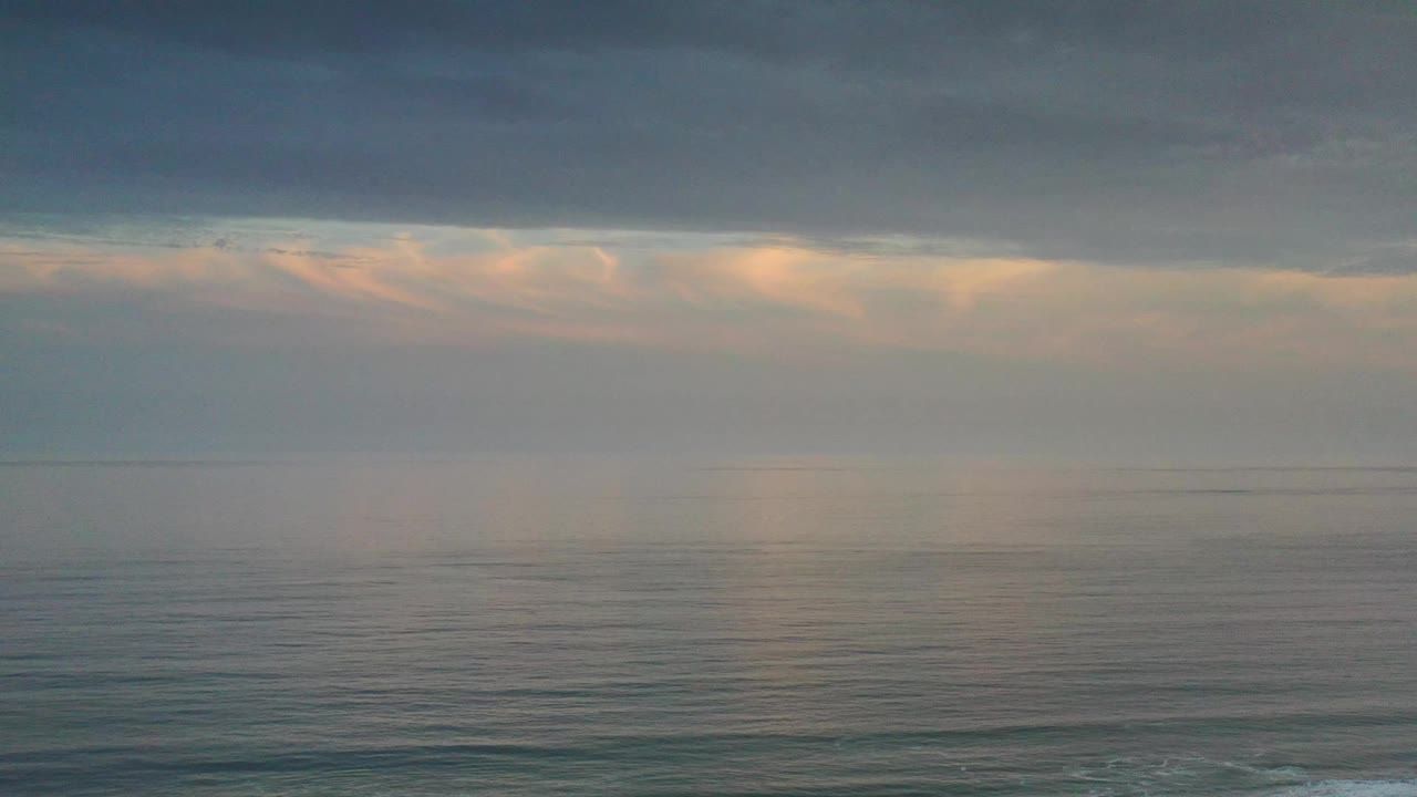 The Los Cabos ocean remains broad and empty as faint peach light shows under the dark cloud shelf, with no visible people or boats.