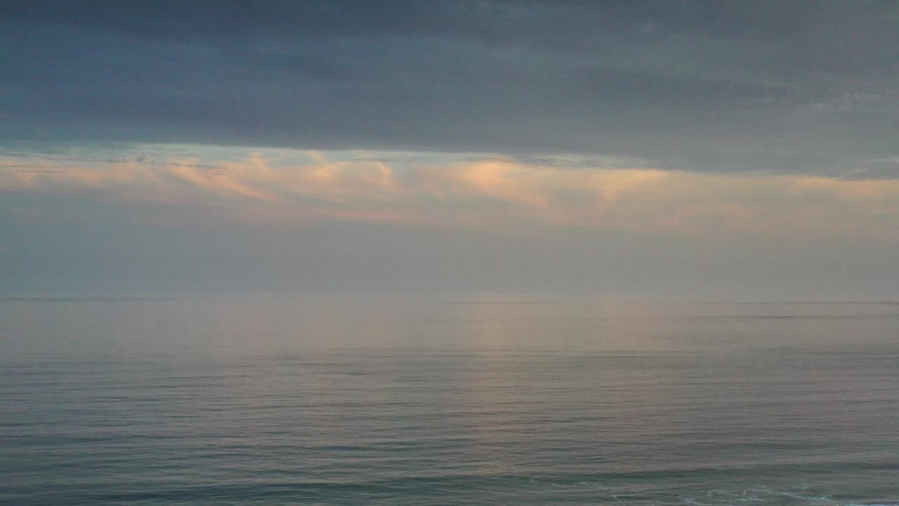 Overcast sea horizon with soft peach light below clouds.