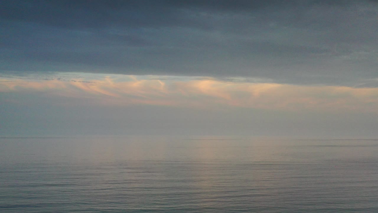 Los Cabos ocean horizon under a dark blue-gray cloud layer, with warm sunlight breaking through near the horizon and no visible people.