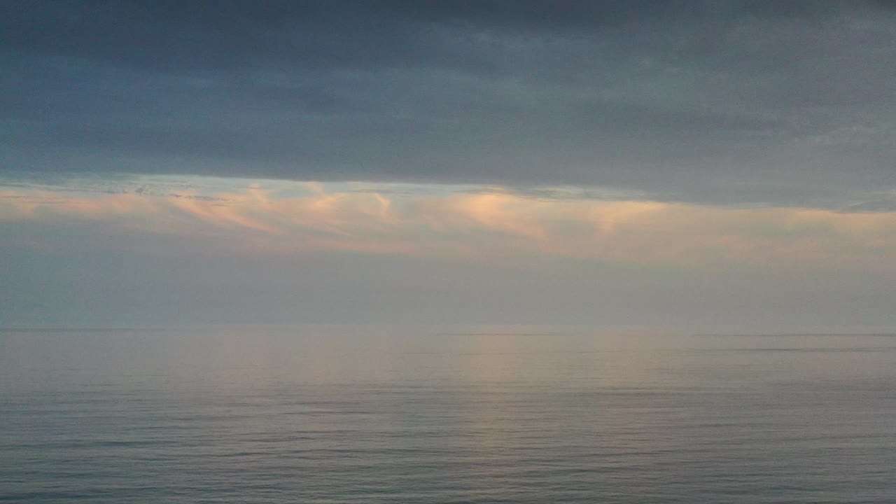 Blue-gray sky over ocean with a thin bright opening near the horizon