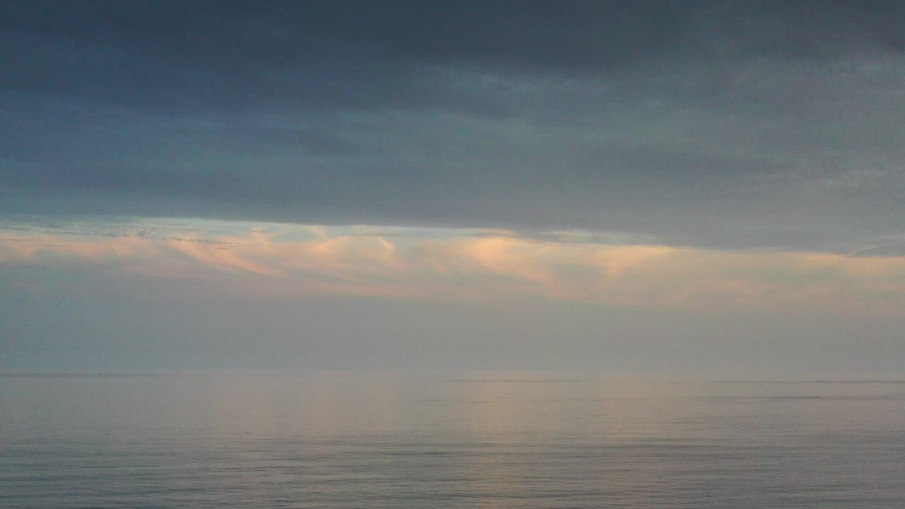 Los Cabos ocean horizon under a dark cloud shelf, with pale warm light diffused through mist and no visible people.