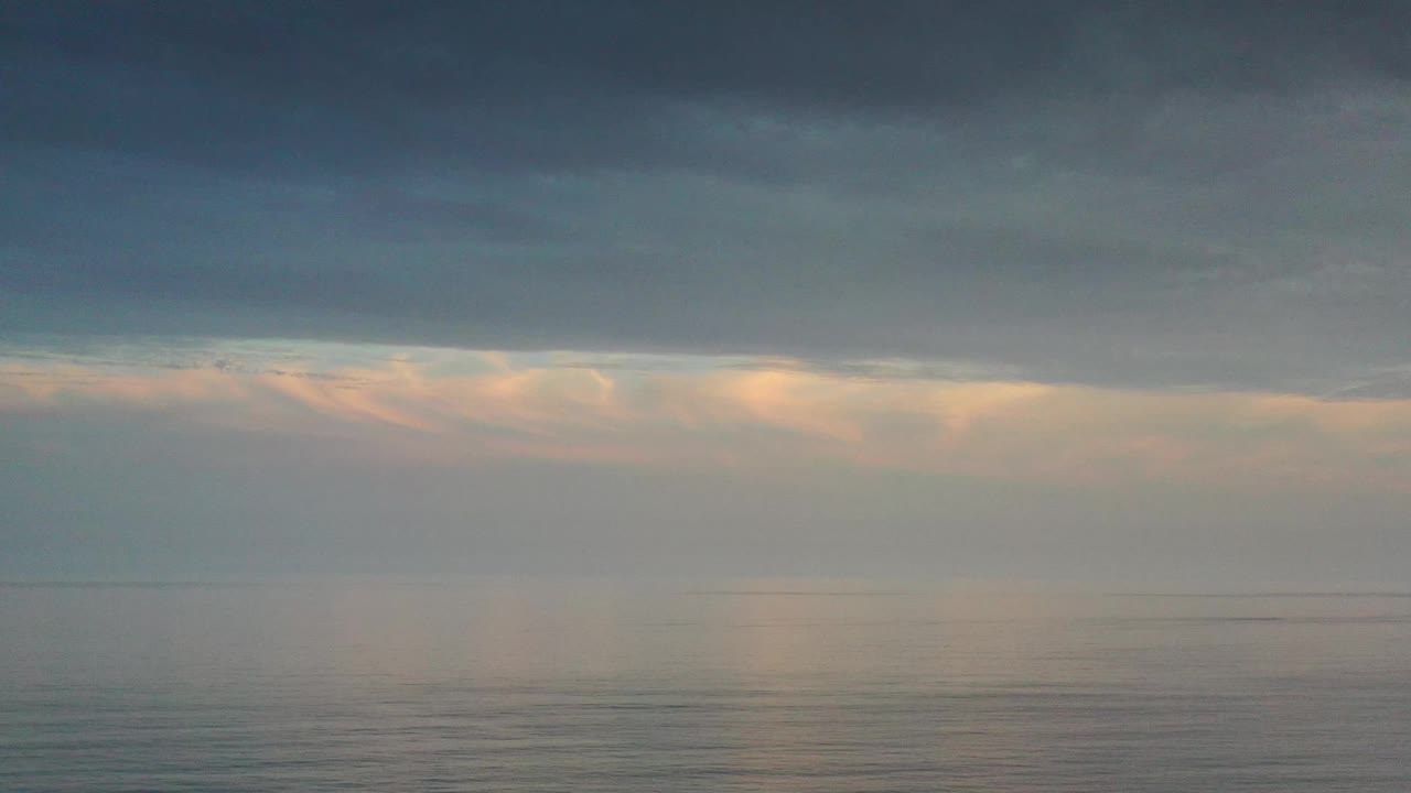 Aerial view over the Los Cabos ocean with a broad gray cloud bank, thin fog near the horizon, and no visible people.