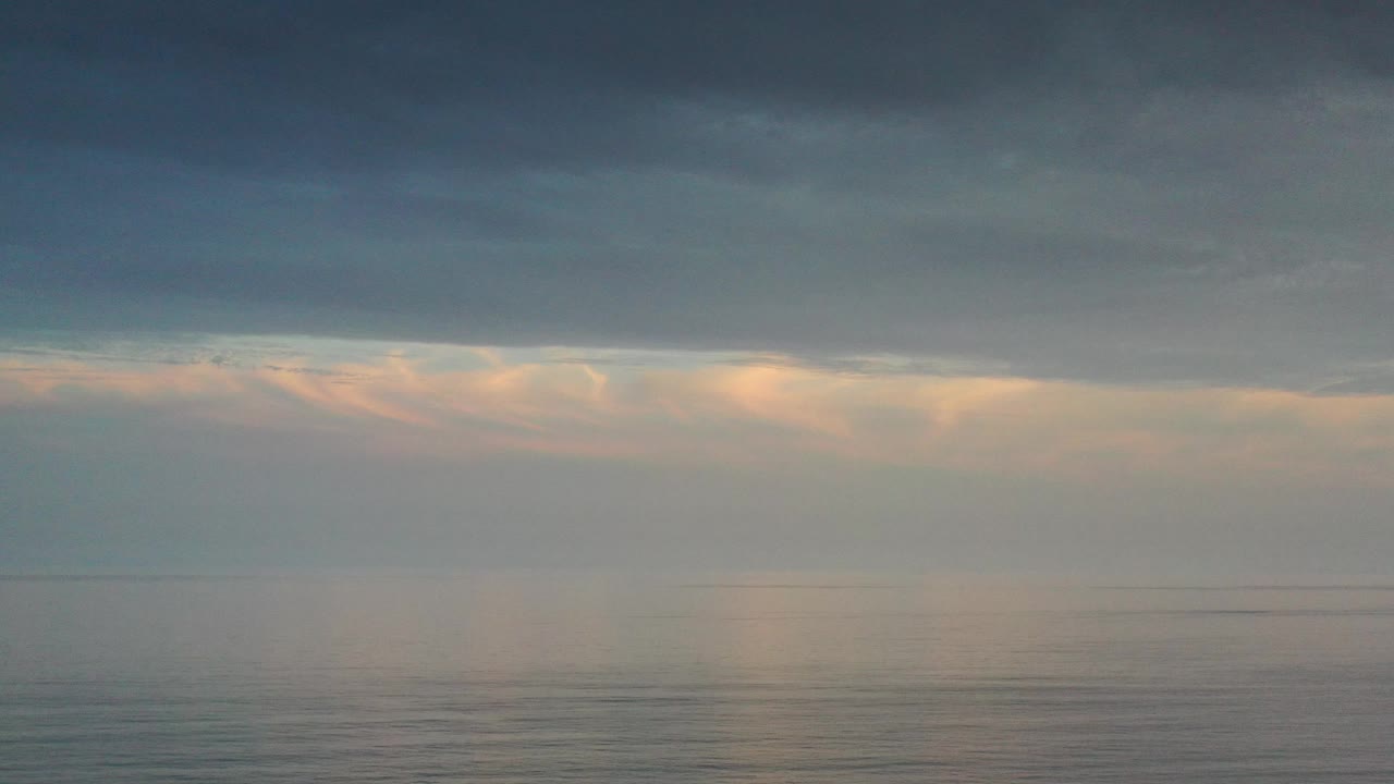 Muted sea surface with low clouds and warm breaks of light.