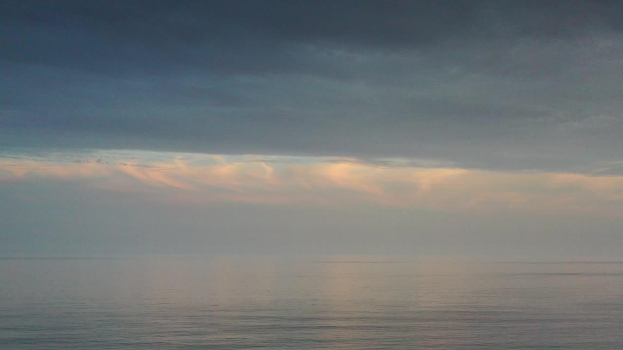 Cloudy sunset sky reflected on calm sea.