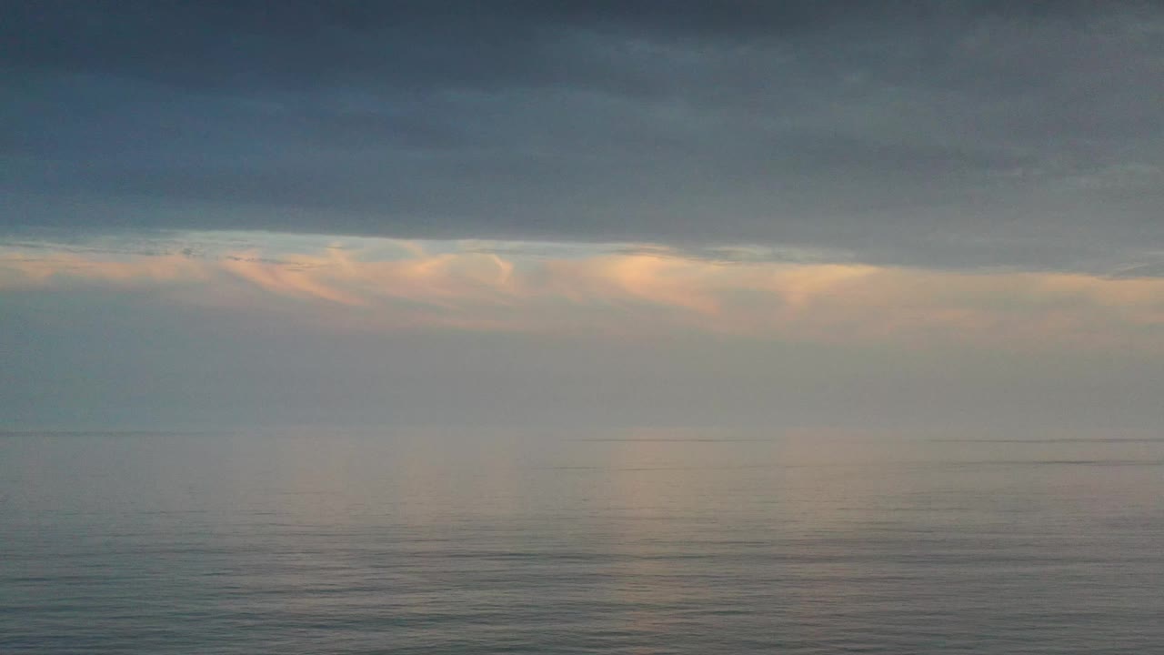 Los Cabos sea and sky fill the frame, with a low horizon, gentle surface texture, peach-lit cloud tops, and no visible people.