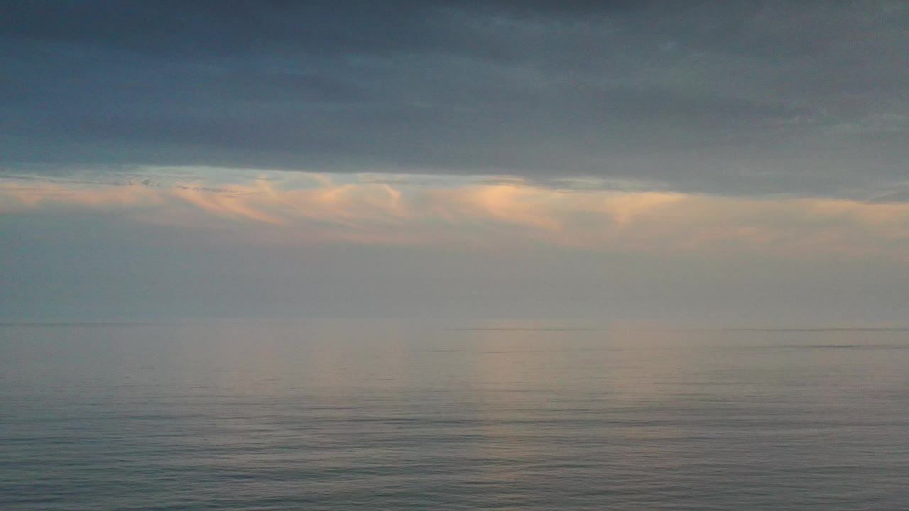 Open ocean under a gray cloud shelf with warm light near the horizon.