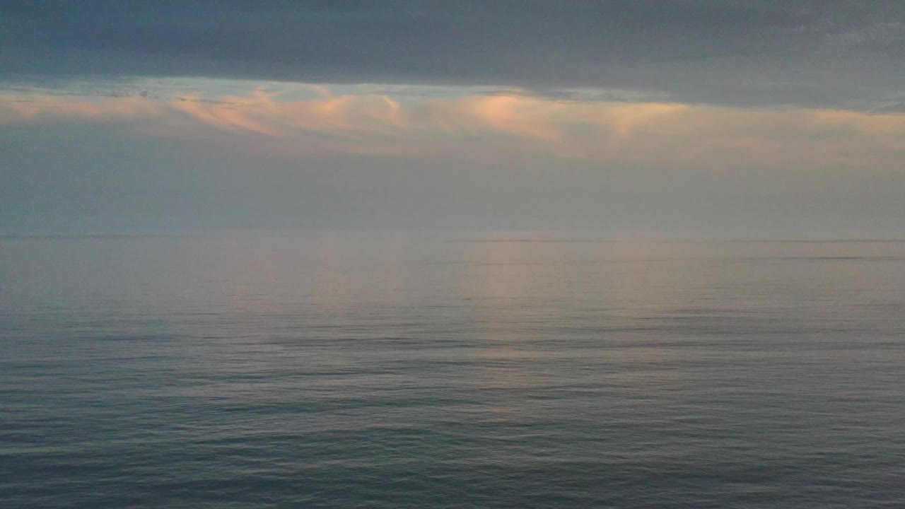 Los Cabos ocean surface one second in, showing faint light reflection on gently rippled water beneath a gray cloud layer, with no visible people.