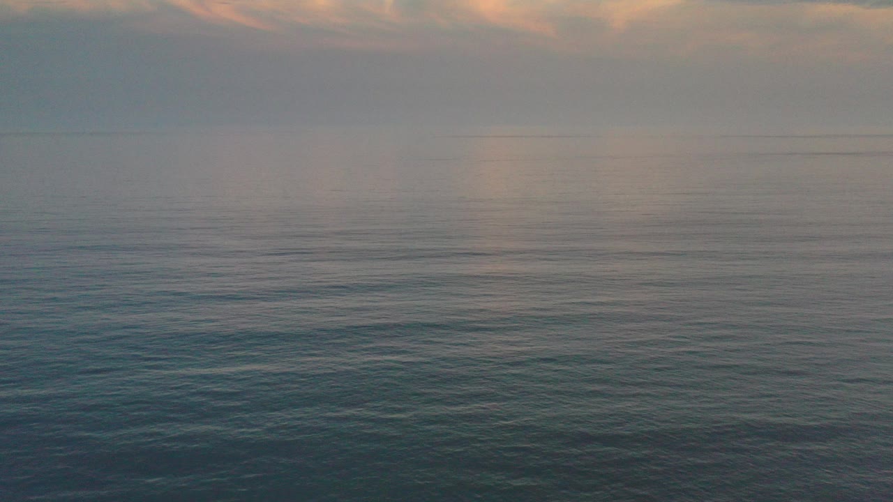 Calm ocean under a hazy sunrise sky.