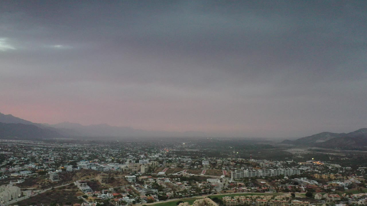 Wide aerial view of a city below mountains and heavy clouds.