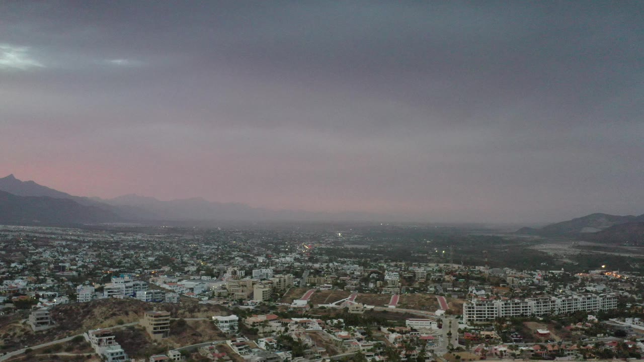 Hazy cityscape with desert hills, distant mountains, and low cloud cover.