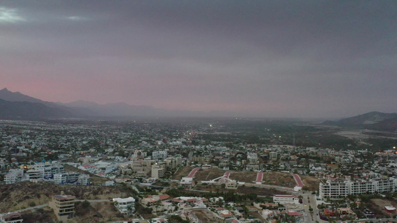 Wide aerial view of a city under heavy clouds and distant mountains.
