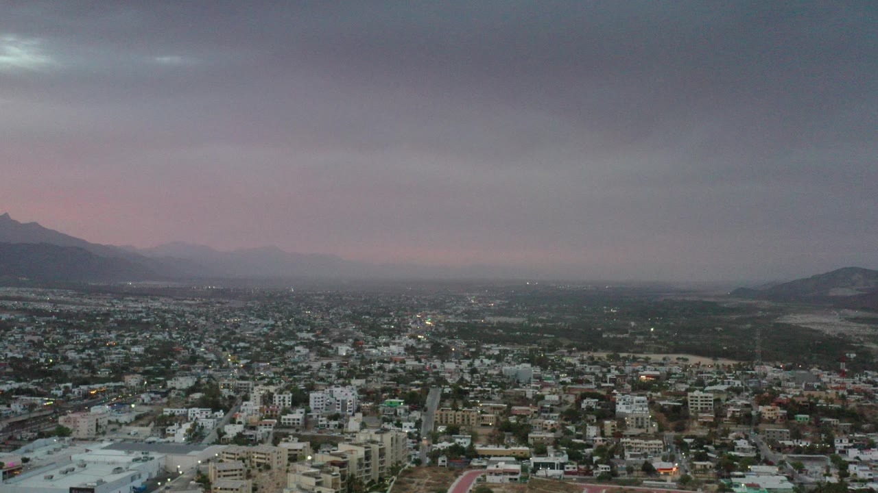 Suburban town beneath dark clouds and distant mountains.