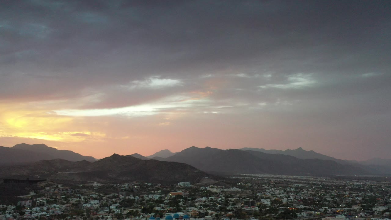Sunset over mountains and a city below dark clouds.