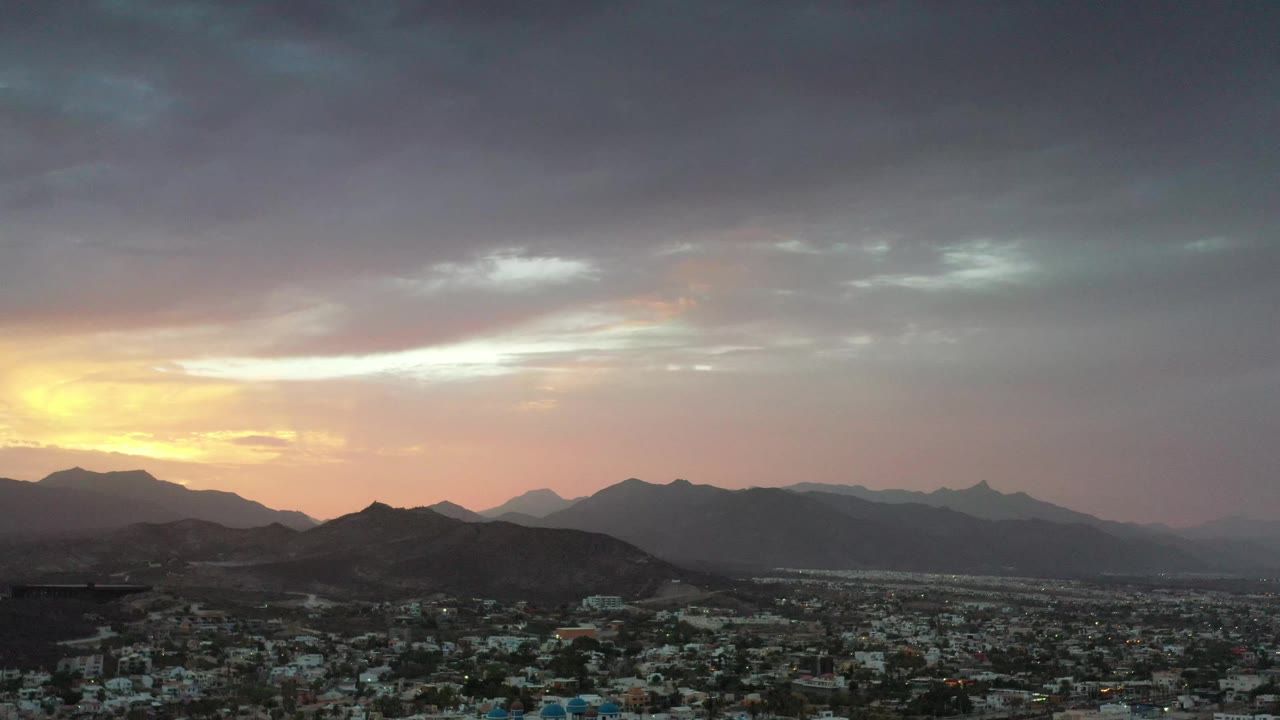 Los Cabos, Mexico skyline with the sun glow low on the left, dark hills in the center, hazy distant peaks to the right, and no visible people.