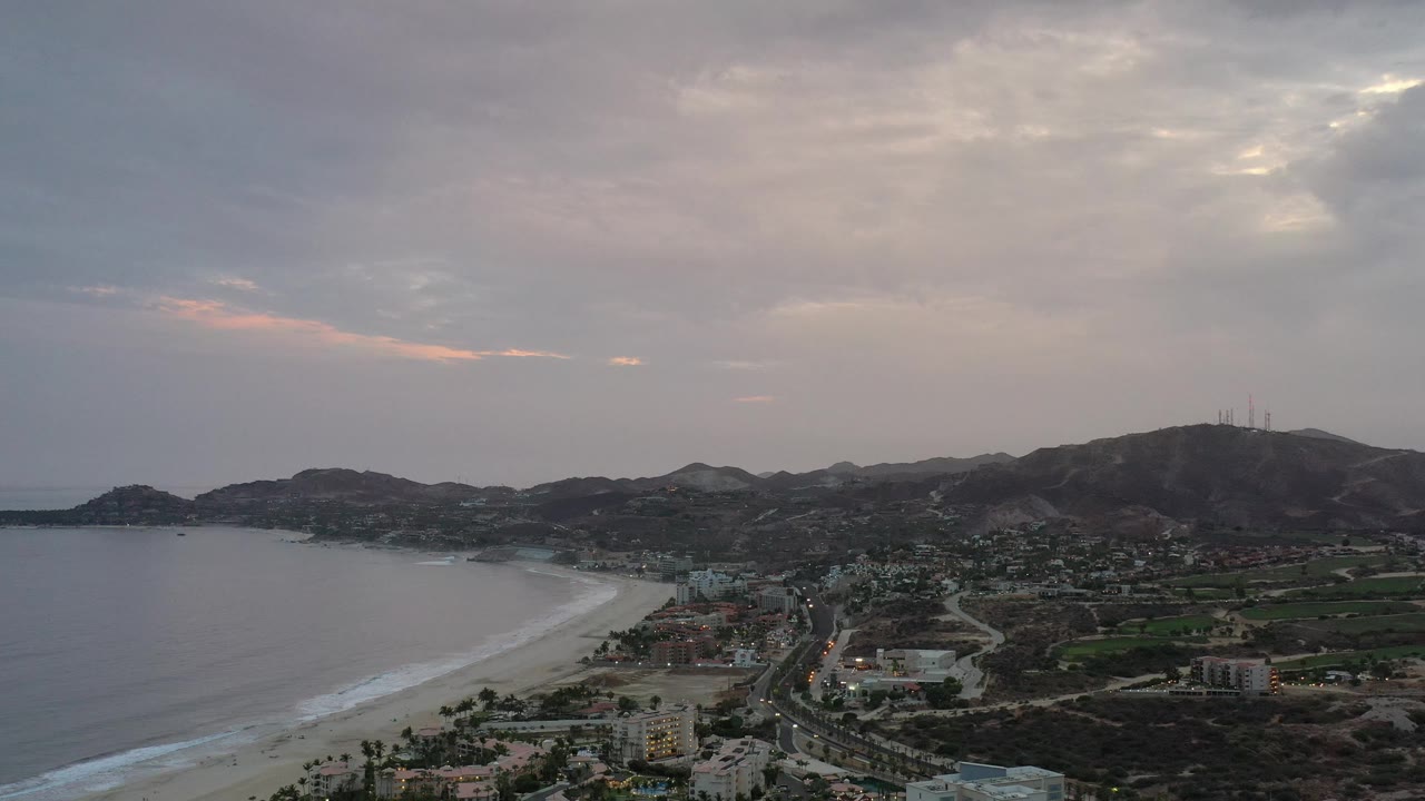 Coastal aerial with beach on the left and mountain ridge under gray clouds.