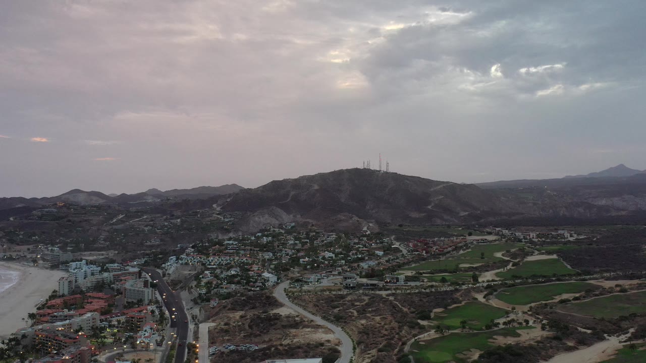 Aerial city and mountain view under gray clouds with roads and fields below.