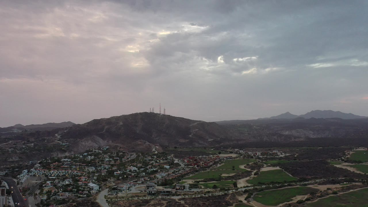 Aerial view of homes, green fields, hills, and cloudy sky.