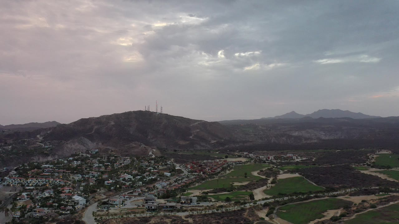Wide aerial view of houses, roads, fields, hills, and a cloudy dawn sky.