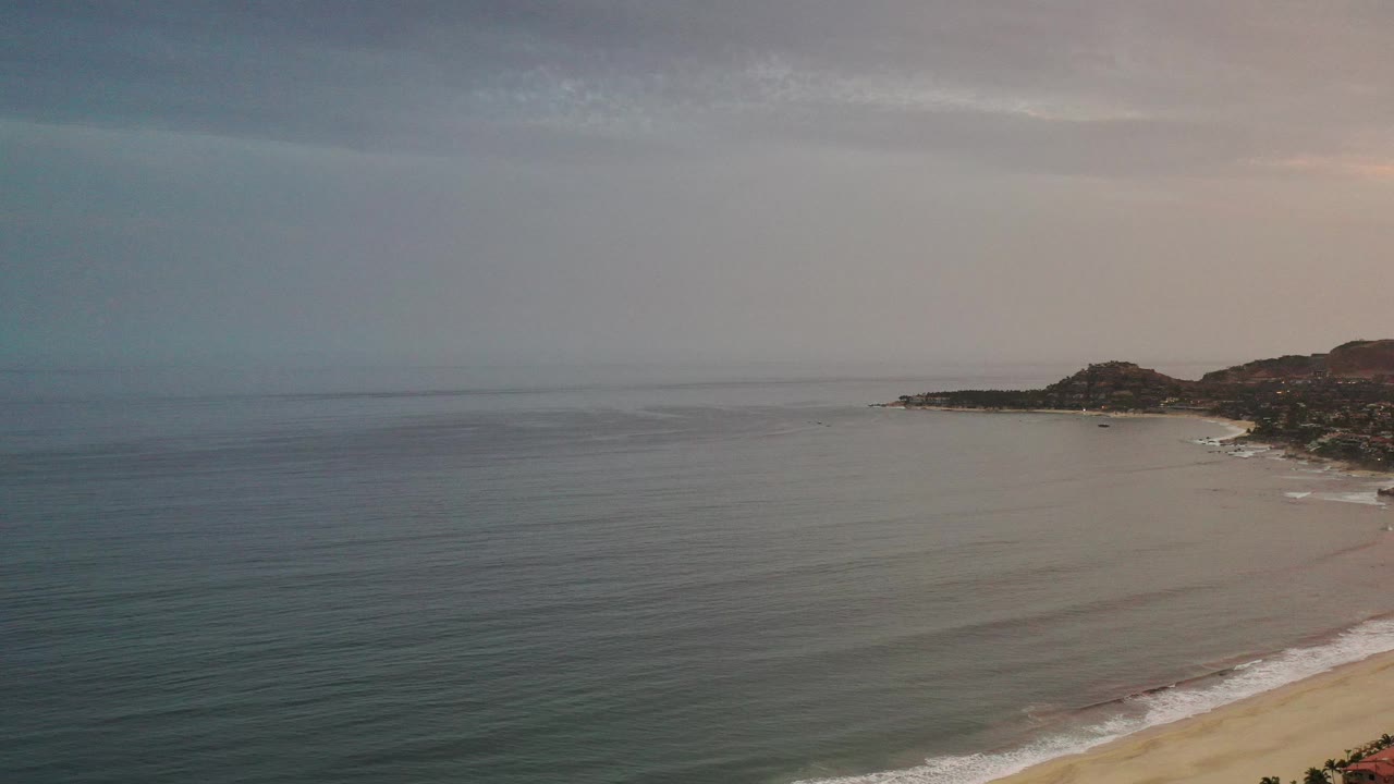High view of calm ocean and curving beach below distant hills