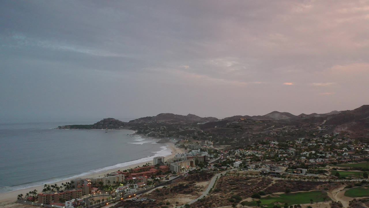 High coastal view with beach, clustered buildings, roads, and hills.