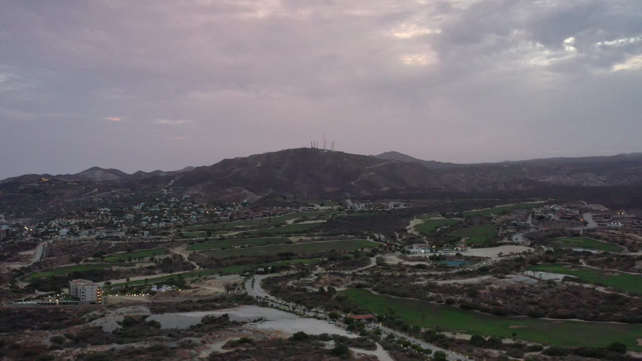 Aerial view of hills, fields, roads, and scattered buildings under cloudy sky.