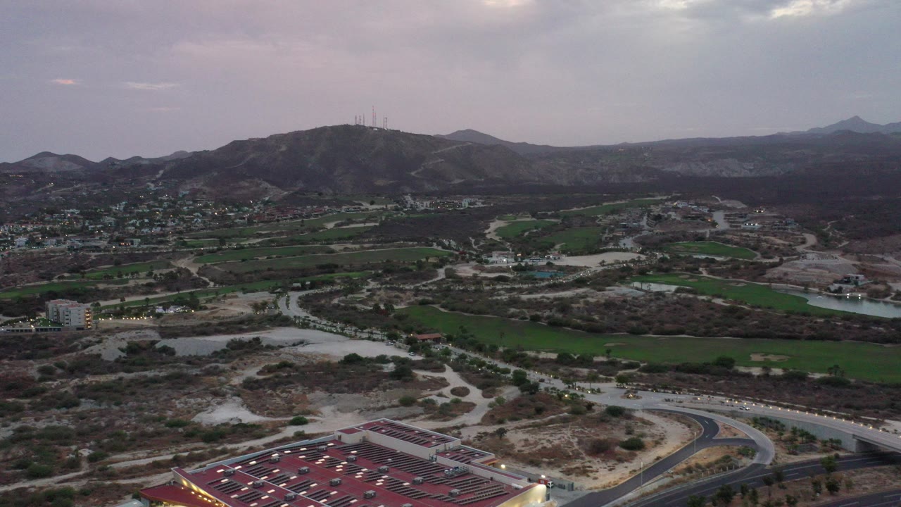 Wide aerial view of roads, fields, buildings, hills, and distant mountains.