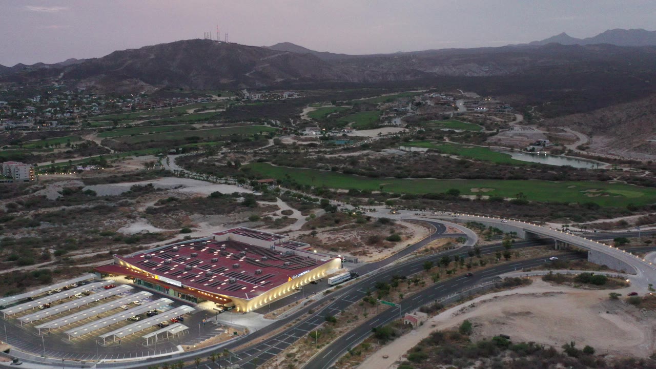 Aerial view of a lit red-roofed building, roads, green fields, and mountains.