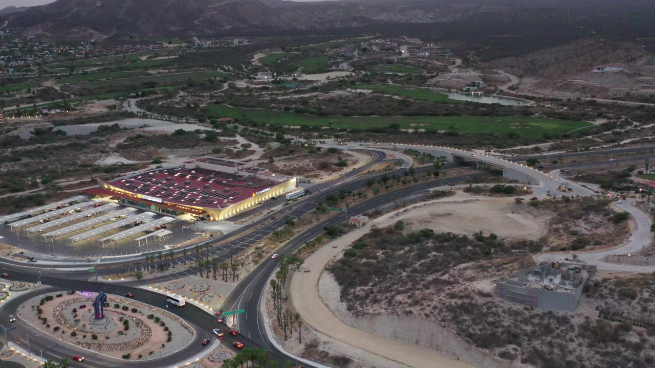Aerial view of a roundabout, roads, lit building, and mountains at dusk.
