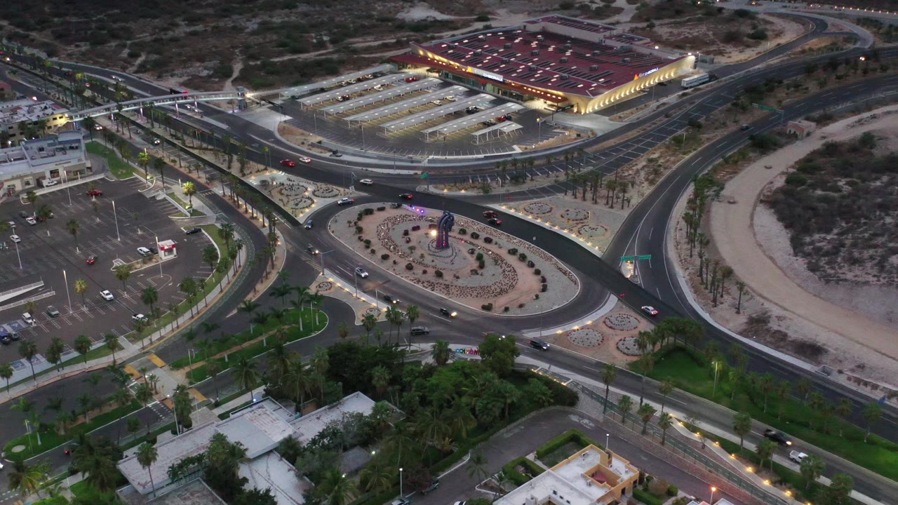 Elevated view of a road junction, landscaped islands, parked cars, and a lit building.