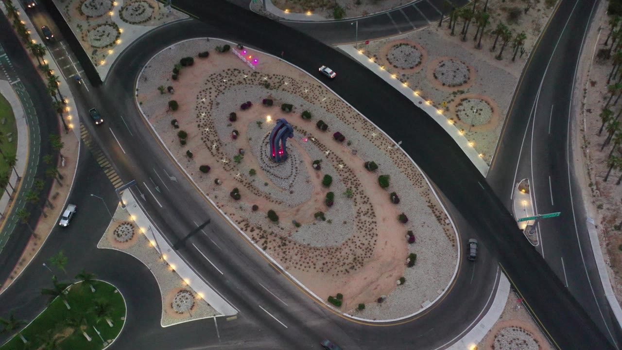 Top-down road loop with cars, planted median, and illuminated roadside landscaping.