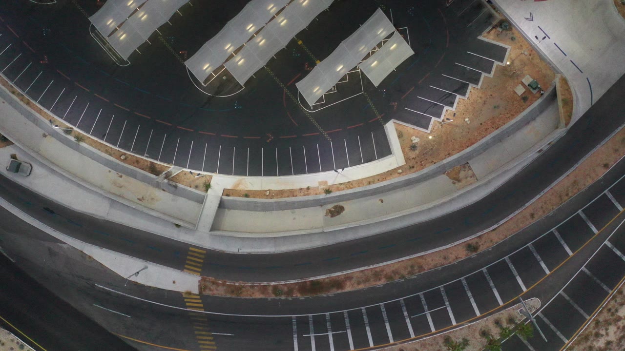 Top-down Los Cabos, Mexico frame showing curved asphalt roads, empty marked parking bays, pale sidewalks, desert landscaping, and no visible people.