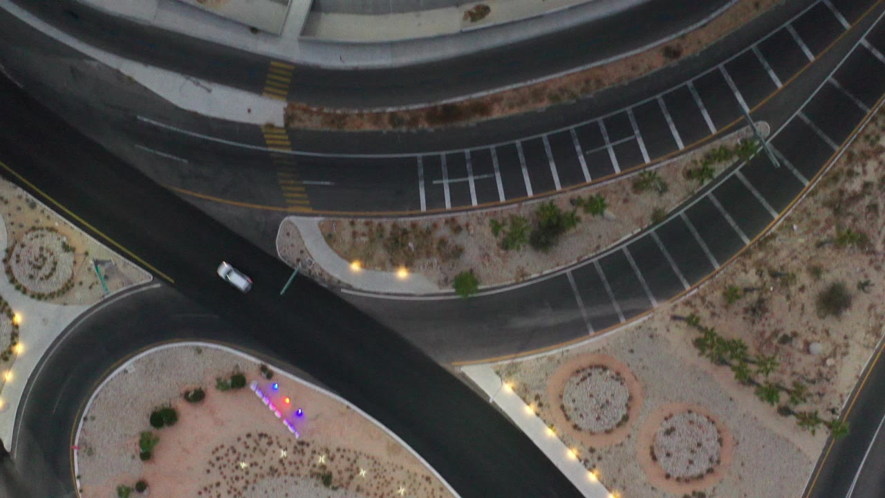 Overhead Los Cabos street view with dark curved roads, desert landscaping, marked parking spaces, warm lights, and no visible people.