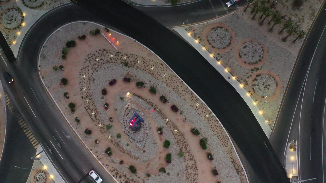 Overhead view of curved roads around a landscaped median with cars and lights.